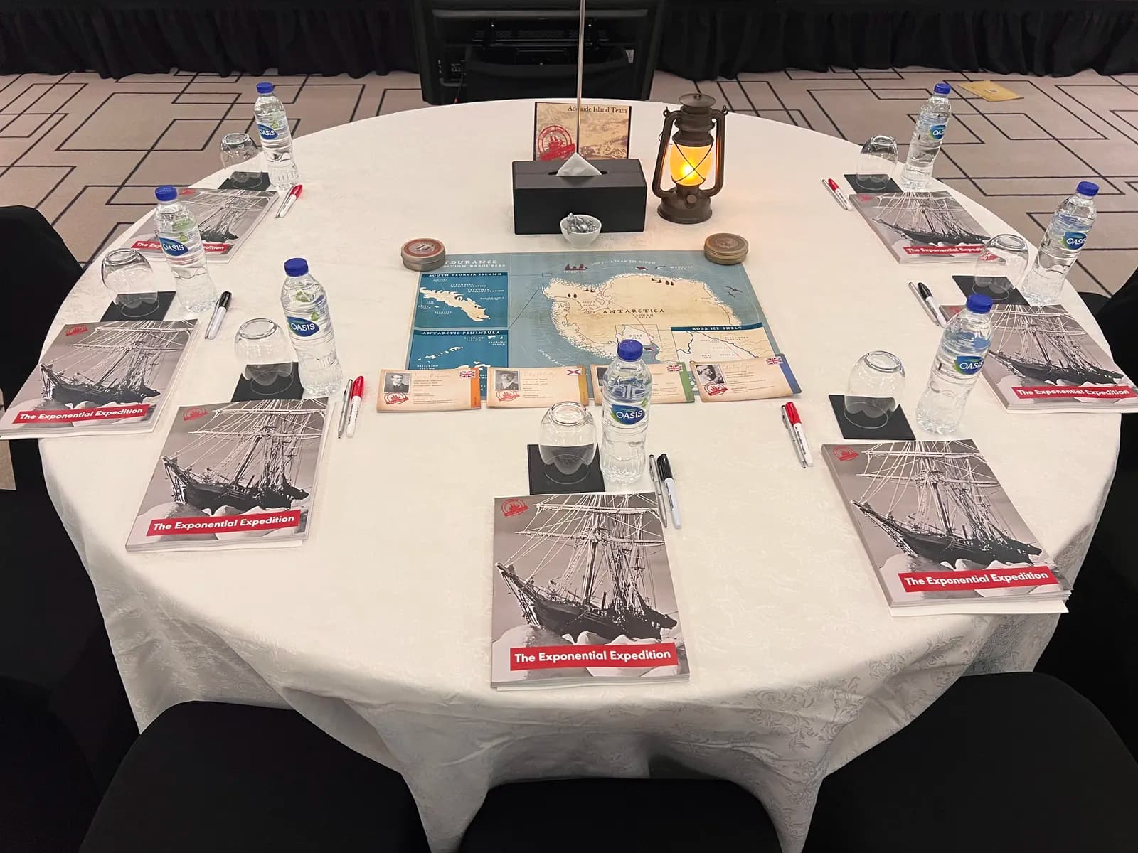Lead the Endurance table setting close-up — The Exponential Expedition workbooks, Antarctica route map, lantern centerpiece, and participant materials